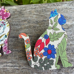 A cat-shaped decorative item with a colourful floral print sits on a weathered wooden surface