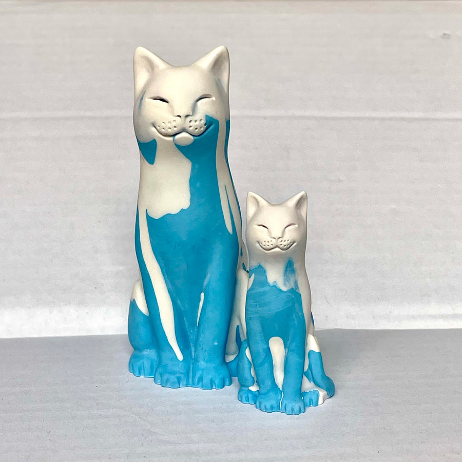 Light Blue and white smiling lucky cat and kitten figurines on a grey surface with a light grey background