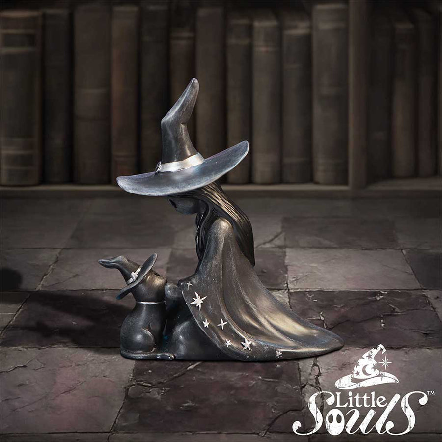 Decorative witch figurine with a hat and cape on a stone floor with books in the background, featuring the brand 'Little Souls'.