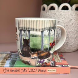 A white ceramic mug with a detailed illustration of two cats lounging by a window