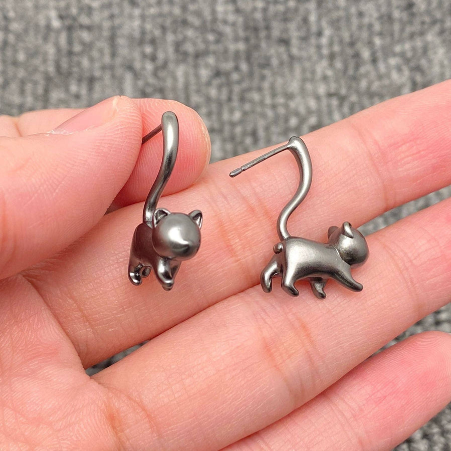 Silver grey cat-shaped earrings held in a hand against a grey background