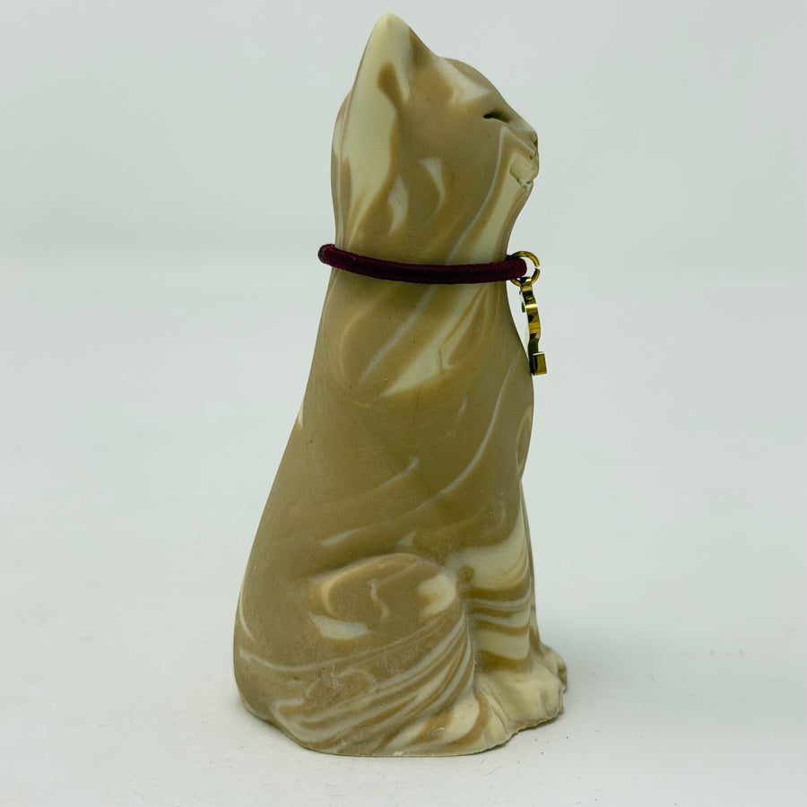 A sculpted lucky cat figurine in a cream and tan marbled stone-like finish, wearing a dark burgundy collar with a small gold charm
