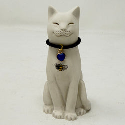 A white resin lucky cat figurine wearing a black collar with a blue heart-shaped pendant and a small bee decoration