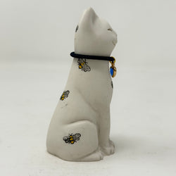 A white resin lucky cat figurine sitting and facing right, decorated with small yellow and black bees and a black collar