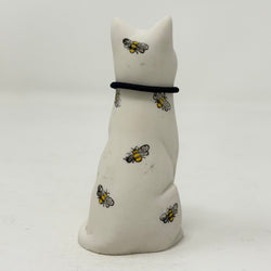A white resin lucky cat figurine with hand-painted yellow and black bees on its back and neck, wearing a black collar.