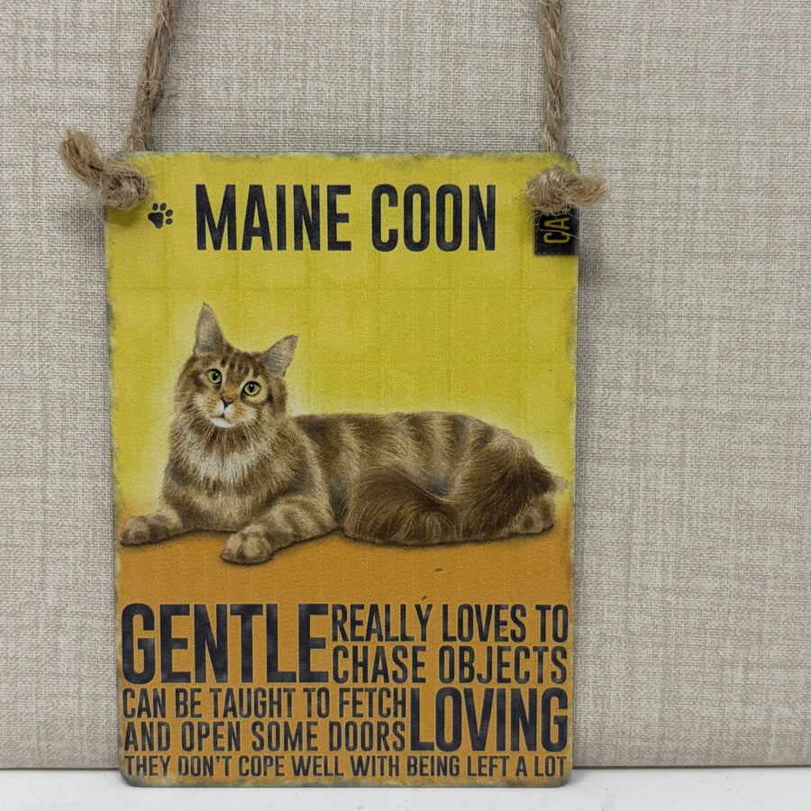 A rectangular hanging sign, featuring a painted Maine Coon cat and humorous text about the breed. The sign is suspended by a rope hanger