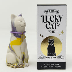 A ceramic Lucky Cat figurine with a white body, purple and yellow stripes, and a purple collar with a gold letter 'P' charm, shown next to its white and gold branded packaging box.