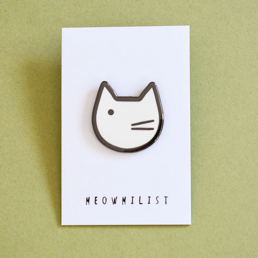 An enamel pin badge with a black and white illustration of a cat's face on a white backing card