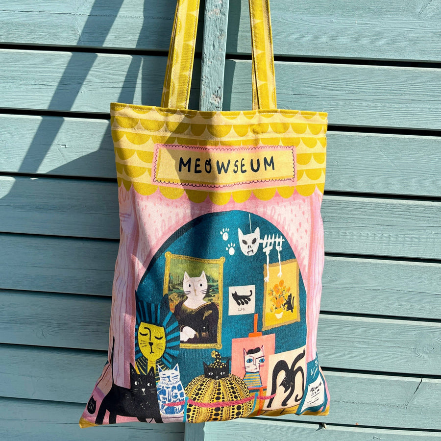 A colourful tote bag with yellow handles. The bag features a whimsical cat-themed illustration with the text 'MEOWSEUM' 