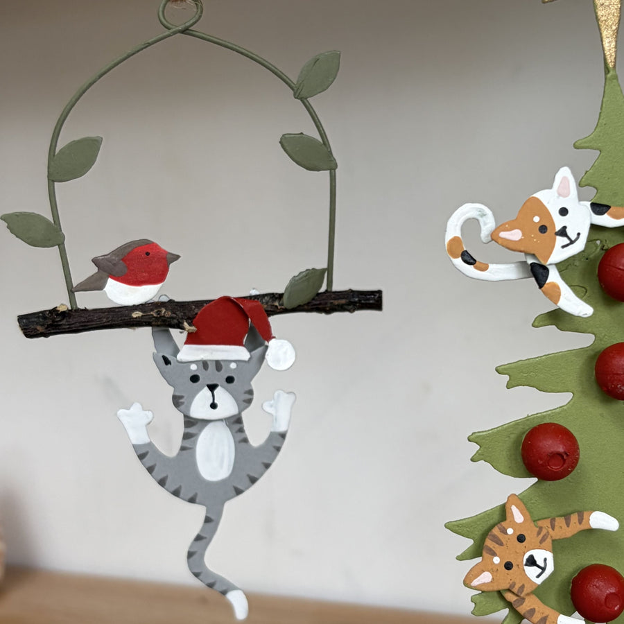 Metal Christmas ornament featuring a grey tabby cat hanging from a branch with a red robin and a Santa hat