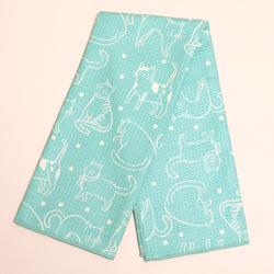 A folded kitchen towel or tea towel in mint green with a white line-art pattern of cats and small white dots, displayed on a light pink background.