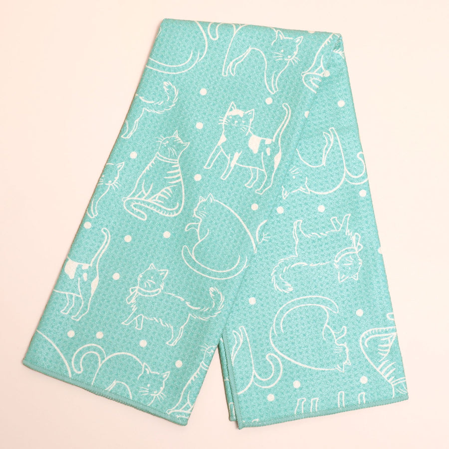 A folded kitchen towel or tea towel in mint green with a white line-art pattern of cats and small white dots, displayed on a light pink background.