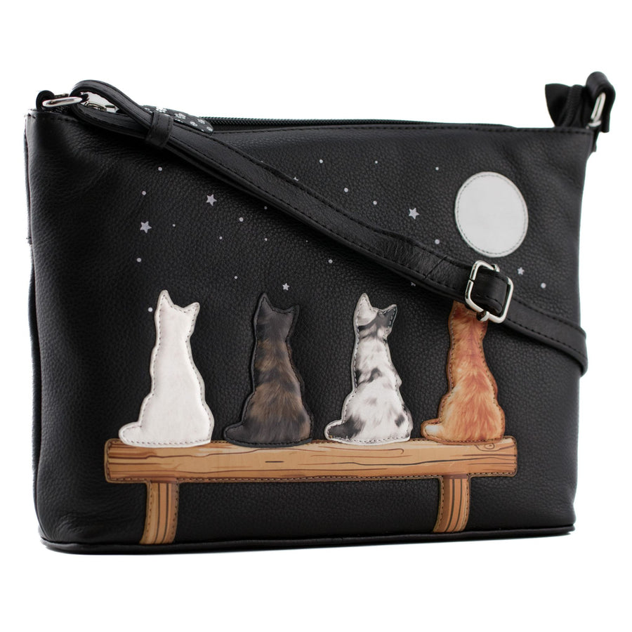 Black pebbled leather crossbody bag featuring a whimsical design of four cats sitting on a wooden bench under a starry night sky with a full moon.