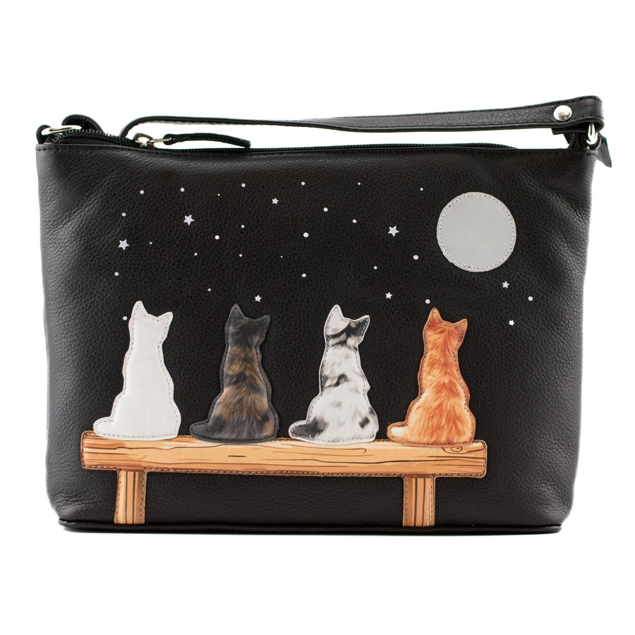 Black leather bag featuring a printed design of four cats sitting on a wooden bench under a full moon and starry night sky.