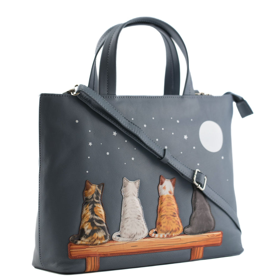 Denim blue leather grab handbag with strap featuring four applique cats on a bench under a moonlit starry sky
