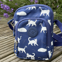 Blue small crossbody bag with white cat pattern on a wooden surface with lavender flowers.