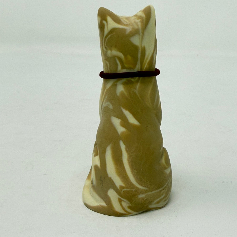 A lucky cat resin figurine shown from the back, coloured in marbled brown and cream with a dark red collar around its neck