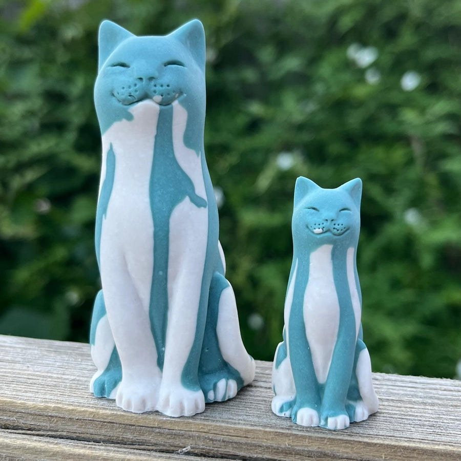 Blue and white lucky cat figurines on a wooden surface with a green foliage background