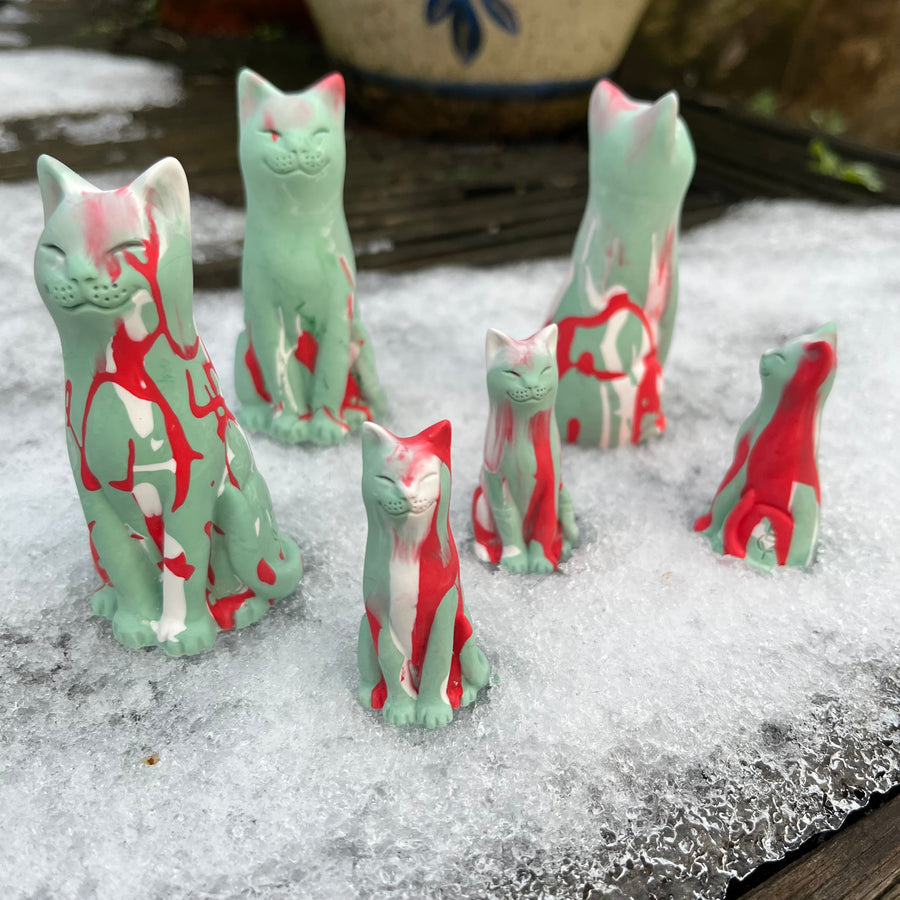 Set of ceramic cat figurines with red and green patterns on a snowy surface.