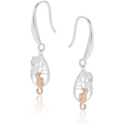 A pair of silver and rose gold dangle earrings with a tree of life design and a rose gold cat, shown on a white background with a soft reflection.