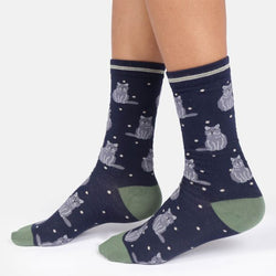 A pair of crew socks worn on a person's feet, featuring a dark navy blue background with a pattern of grey cats sitting on white dots