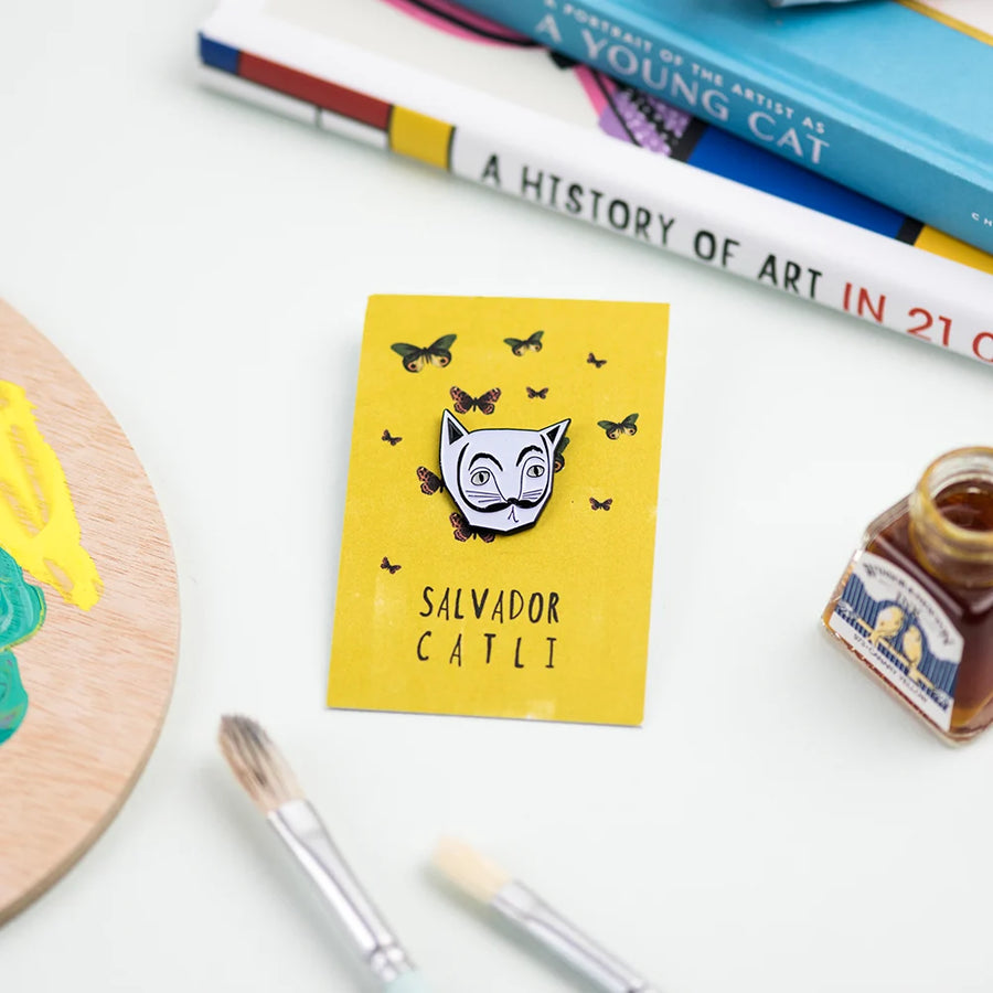 Yellow card labelled Salvator Catli with a white cat pin badge that resembles the artist Salvador Dali