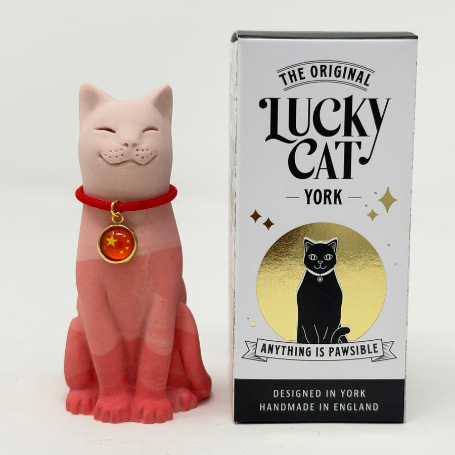 A red gradient Lucky Cat figurine wearing a red collar with a gold medallion, standing next to its white, black, and gold retail box, 'The Original Lucky Cat York'