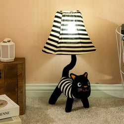Black and white striped cat-shaped lamp with a lampshade on a beige carpet.