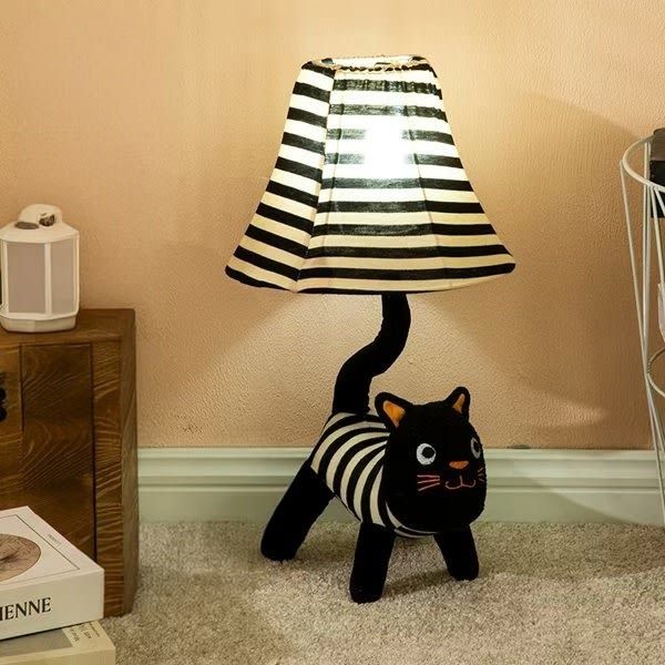 Black and white striped cat-shaped lamp with a lampshade on a beige carpet.