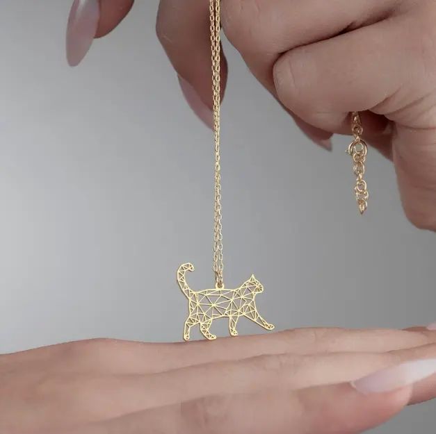 Gold geometric cat pendant on a chain on a persons hand
