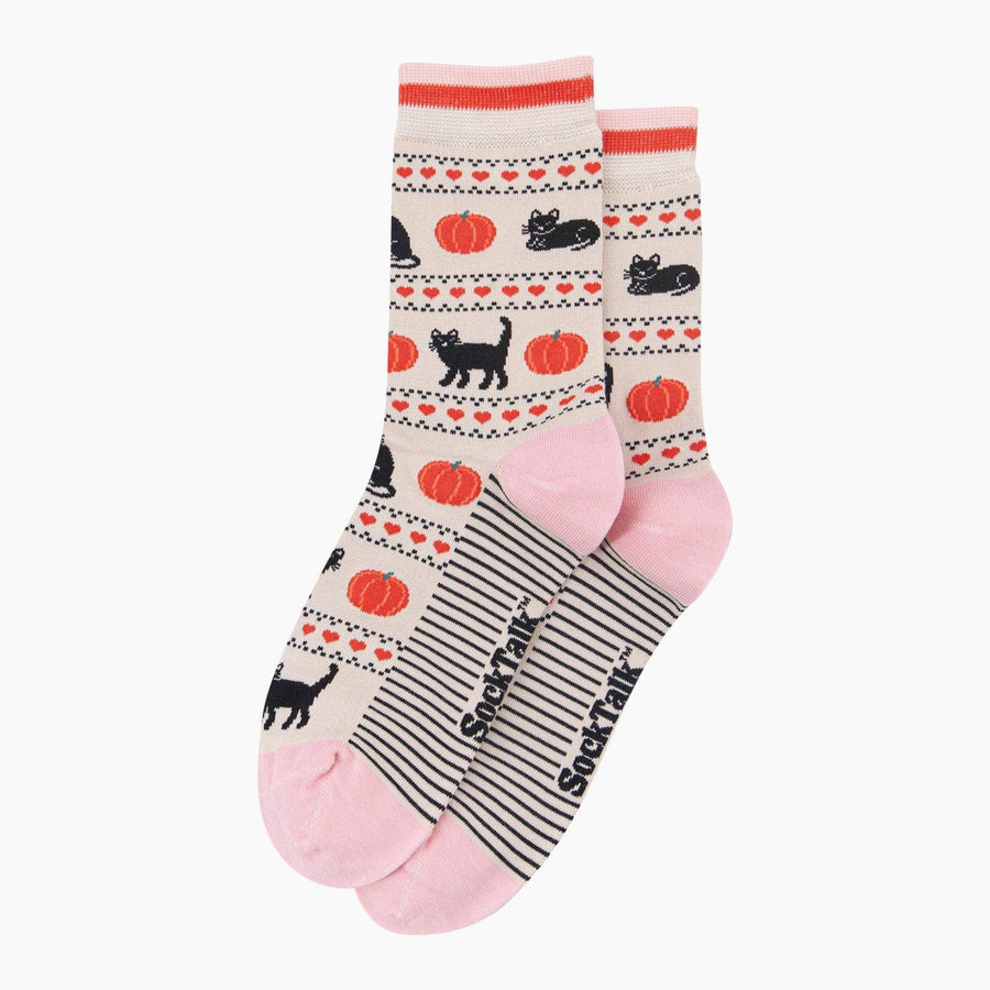 A pair of crew socks with a fall-themed pattern featuring black cats, orange pumpkins, and red hearts on a cream background