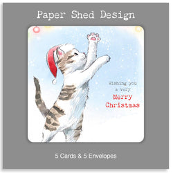A square product card or packaging panel with a grey border and white text reading 'Paper Shed Design' at the top and '5 Cards & 5 Envelopes' at the bottom. The centre shows an illustrated white and grey tabby kitten wearing a red Santa hat, reaching upward against a pale blue snowy background, with red and black Christmas greeting text.