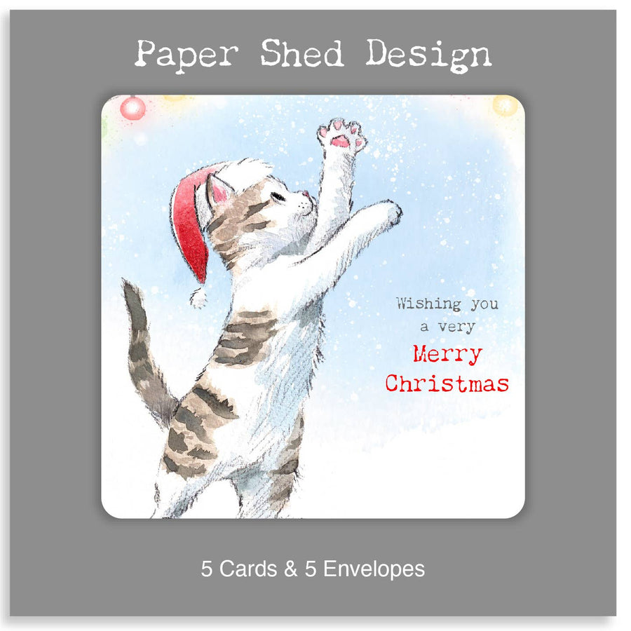 A square product card or packaging panel with a grey border and white text reading 'Paper Shed Design' at the top and '5 Cards & 5 Envelopes' at the bottom. The centre shows an illustrated white and grey tabby kitten wearing a red Santa hat, reaching upward against a pale blue snowy background, with red and black Christmas greeting text.