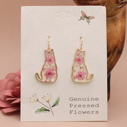 Floral cat-shaped earrings on a card with 'Genuine Pressed Flowers' text, surrounded by pink flowers