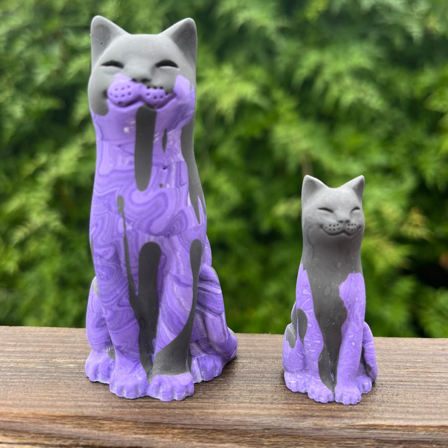 Two purple and black lucky cat figurines on a wooden surface with a blurred green background