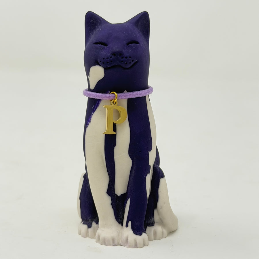 A resin lucky cat figurine with a dark purple and white marbled pattern, wearing a purple collar with a gold letter 'P' charm