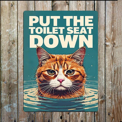 A rectangular metal sign with the phrase “PUT THE TOILET SEAT DOWN” above an illustrated orange tabby cat rising from water