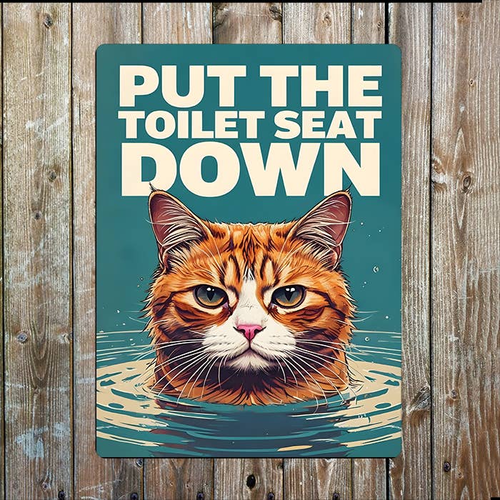 A rectangular metal sign with the phrase “PUT THE TOILET SEAT DOWN” above an illustrated orange tabby cat rising from water
