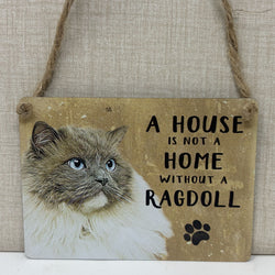 A rustic hanging sign with a photo of a fluffy cat on the left and the text 'A HOUSE IS NOT A HOME WITHOUT A RAGDOLL suspended by twine