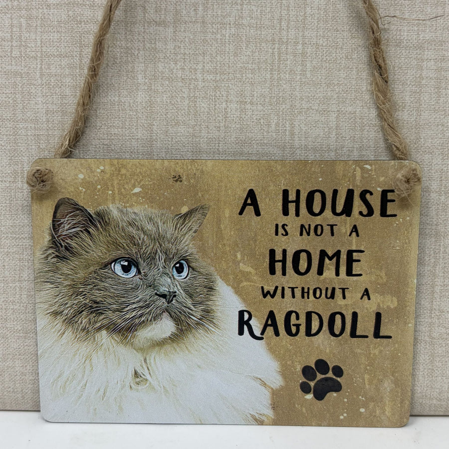 A rustic hanging sign with a photo of a fluffy cat on the left and the text 'A HOUSE IS NOT A HOME WITHOUT A RAGDOLL suspended by twine