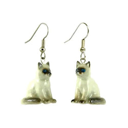 A pair of porcelain earrings shaped like cats with blue painted eyes, attached to surgical steel hooks