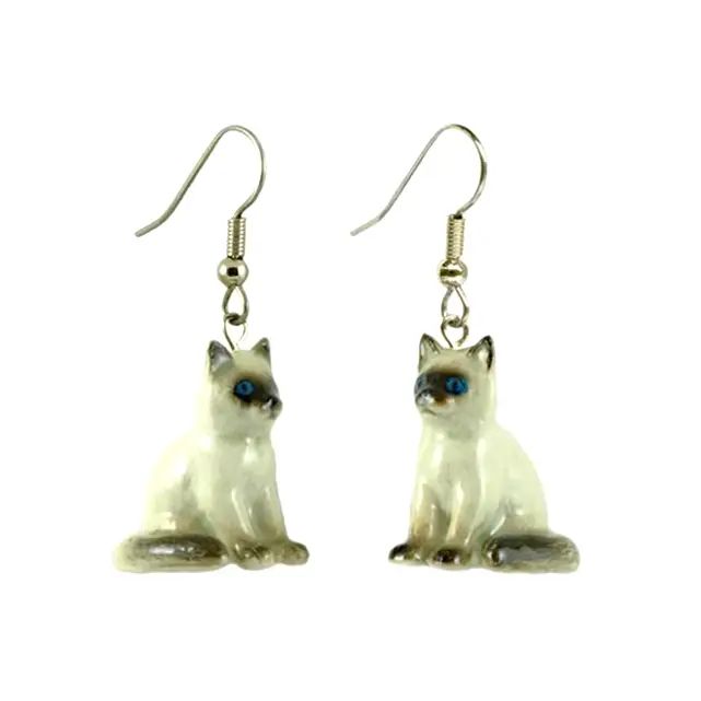 A pair of porcelain earrings shaped like cats with blue painted eyes, attached to surgical steel hooks