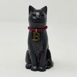 A black lucky cat figurine with multicolor glitter speckles, wearing a dark red collar with a gold initial 'B' pendant