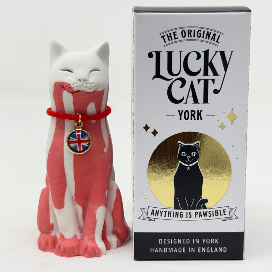 A white and red lucky cat figurine wearing a red collar with a Union Jack charm, standing next to its white, black, and gold retail box labeled 'The Original Lucky Cat York'.