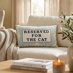 A decorative rectangular pillow with the words 'RESERVED FOR THE CAT' on a cream centre panel, surrounded by a pale blue floral border