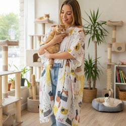 A woman in a cat-friendly home holds an orange tabby cat, wearing a white kimono-style cardigan with a colourful cat print