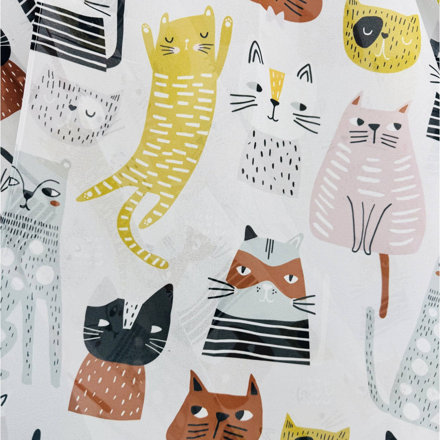 White fabric with a playful pattern of stylized cartoon cats in yellow, orange, pink, black, and gray, some wearing striped shirts