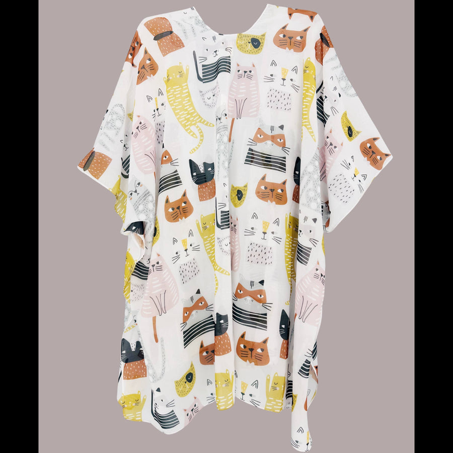A loose, short-sleeved kaftan-style tunic dress with a white base and a playful print of cartoon cats in orange, yellow, black, and pink