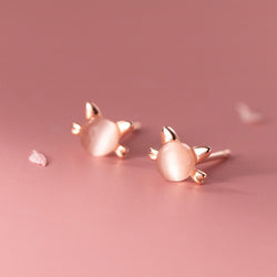 Rose gold cat-shaped earrings on a pink background