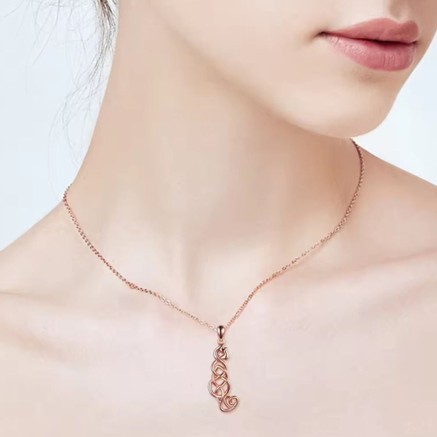 A close-up of a model's neck and lower face wearing a delicate rose gold chain with a matching stylised pendant